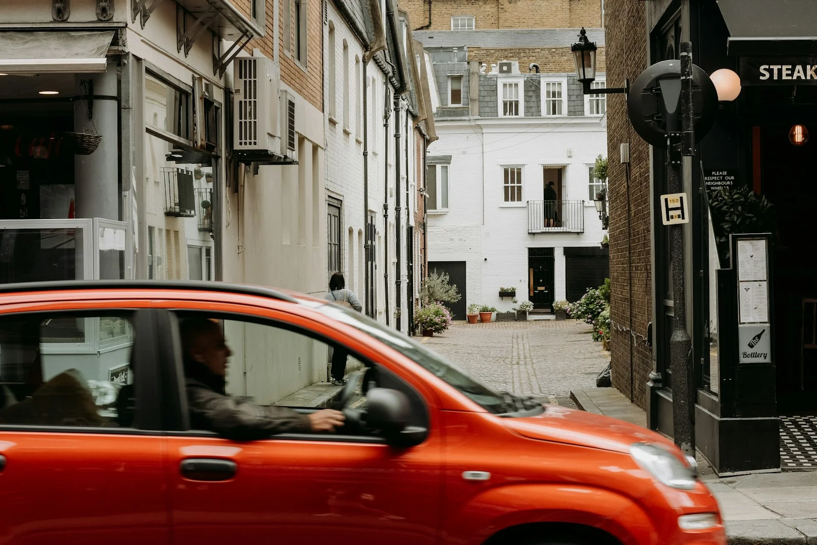 a red car driving down a street next to tall buildings
