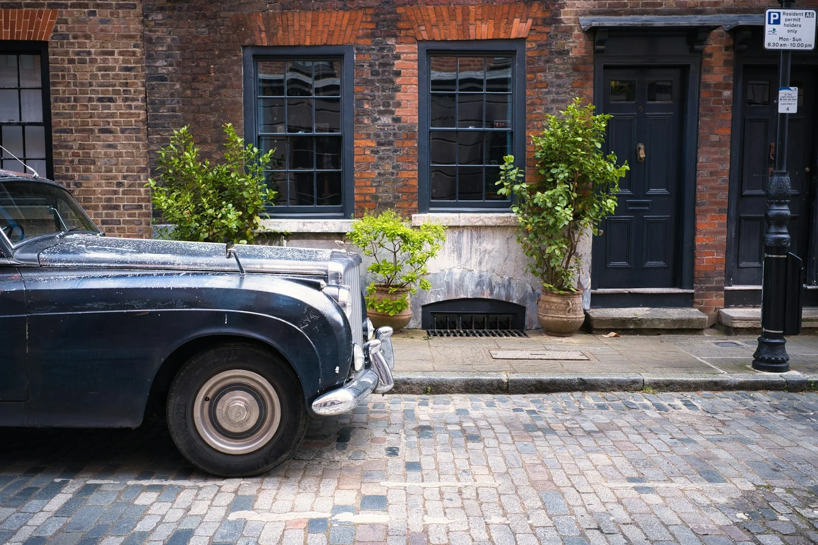 Vintage car parked on cobblestone street outside brick building