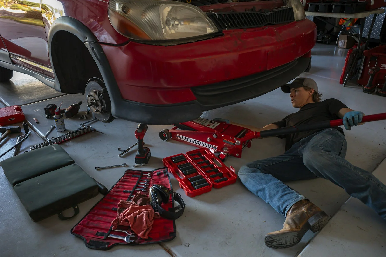 Mechanic lying beside a jacked-up car with tools laid out, checking the wheels and tyres
